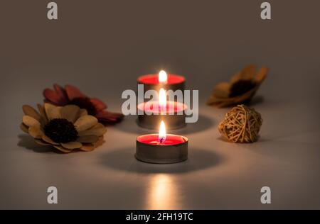 Burning fire of candles on s table. Blurred reflection and selective focus of glowing candle flames in white table surface with artificial flowers dec Stock Photo