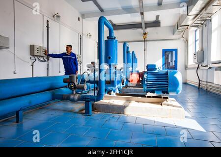 Water purification station, Shardara river. Asian worker control water pumps. Blue industrial tiles floor. Kyzylorda, Kazakhstan. Stock Photo