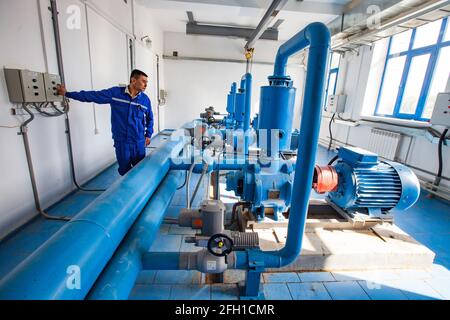 Kyzylorda, Kazakhstan: Water purification station. Asian worker control water pumps. Blue pipe on foreground, sun light. Blue tile floor. Stock Photo