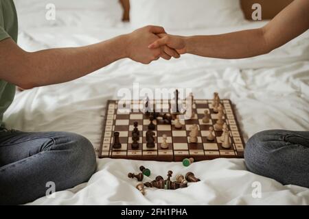 Happy young couple is shaking hands in bed with chess on it. Young family moving to new apartment Stock Photo