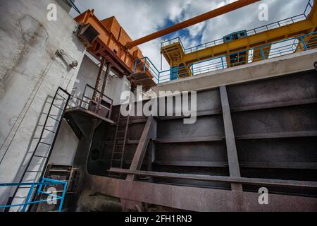 Lifting mechanism of water shutter. Shardara river dam. Grey metal shutter and yellow overhead crane. Kazaly city, Kyzylorda region, Kazakhstan. Stock Photo