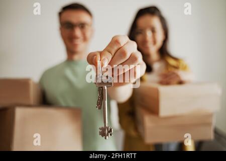 Close up happy couple holding keys of new apartment with boxes. Young family moving to new apartment Stock Photo