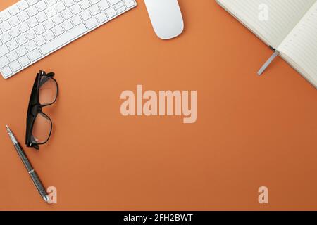 Glasses white keyboard mouse pen and diary on orange background Stock Photo