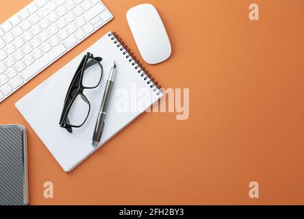 Glasses keyboard mouse pen notepad and diary on orange background Stock Photo