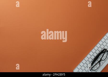 Glasses and white keyboard on orange background Stock Photo