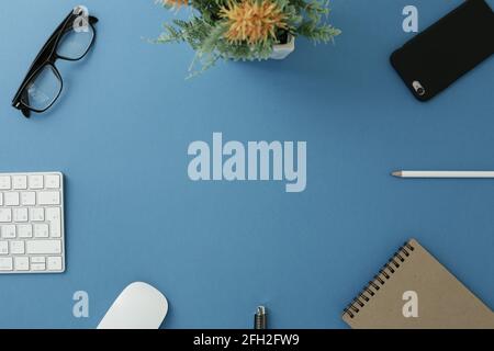 Glasses white keyboard flower notepad mouse pen pencil and phone on blue background Stock Photo