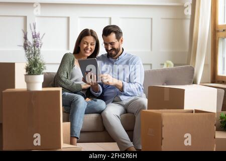 Happy couple relax on sofa using tablet on relocation day Stock Photo
