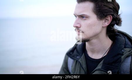 Attractive blue eyed young man with beard and curly hair lone portrait on coast Stock Photo