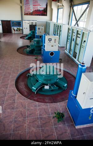 Hydroelectric power plant machine room.Three green electric generators.Control panels,indicator lamps,switchers, buttons.Grey power electric cabinets. Stock Photo