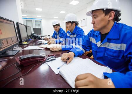 Moinak hydroelectric power station, control room. Three Asian operators supervising processes. Right man blurred, center man in focus. Stock Photo