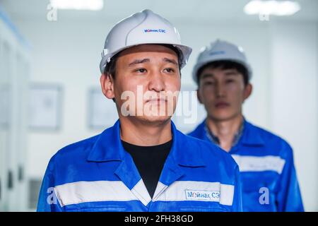 Moinak hydroelectric power station. Two young Asian operators posing. Left in focus, right blurred in shadow. White hardhats, blue workwear. Stock Photo