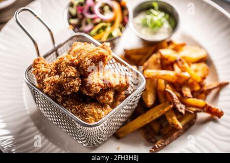 Fried chicken nuggets in metal basket served with french fries on a white plate. Stock Photo