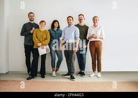 Successful creative team standing against wall looking at camera. Colleagues standing at wall in office. Stock Photo