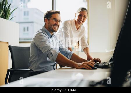 business partners working together on computer. Colleagues smiling and discussing project on computer. Stock Photo