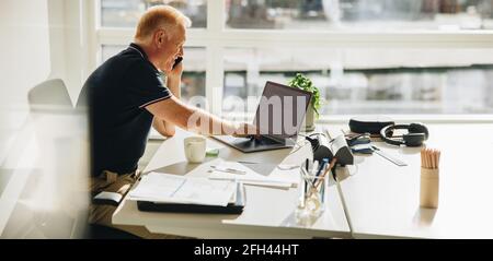 businessman talking over phone while working on laptop. Man sitting with a laptop computer talking over cell phone. Stock Photo