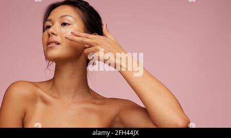 Asian woman applying anti-aging cream on her face. Pretty woman putting cosmetic cream on her face. Stock Photo