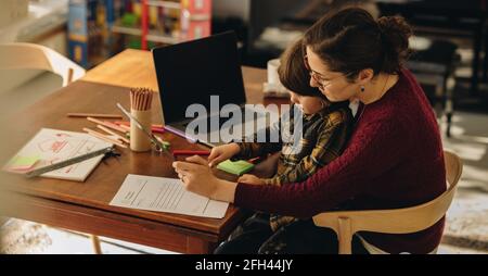 Kid using digital tablet while sitting on lap of his mother. Woman with son drawing in graphic table using stylus pen. Stock Photo