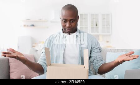 Home delivery. Shocked african american man spreading his hands, having problem, getting wrong order or empty box Stock Photo