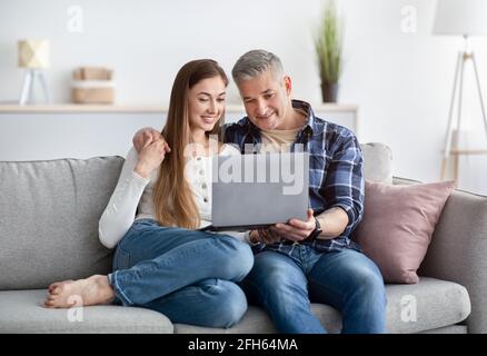 Happy mature couple sitting on sofa with laptop computer, chatting to friend or family online, indoors Stock Photo