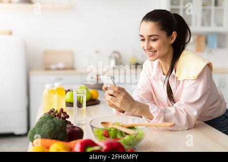 Portrait of smiling young woman using cellphone in kitchen Stock Photo