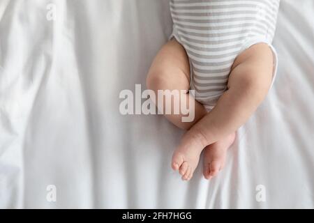 Cropped Image Of Little Baby In Diaper And Bodysuit Lying On Bed Stock Photo