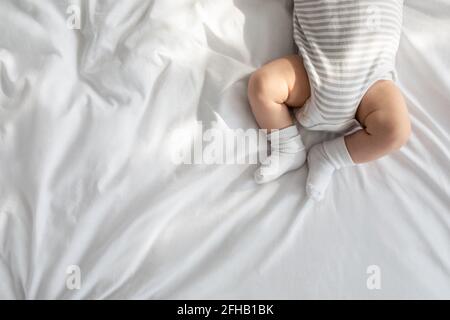 Top View Of Newborn Baby In Bodysuit And Socks Lying On Bed Stock Photo