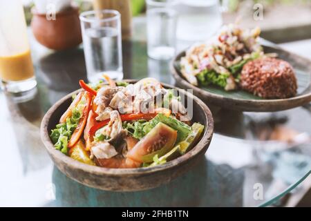 Delicious healthy chicken salad with tomatoes and capsicums served on glass table near plate with healthy black rice in Asian restaurant Stock Photo