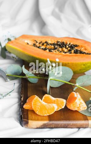 Half of pawpaw with seeds between tangerines and cumquats with leaves on white crumpled cloth Stock Photo