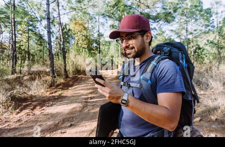 African American bearded male with dreadlocks and upped hands smoking cigar near trees Stock Photo