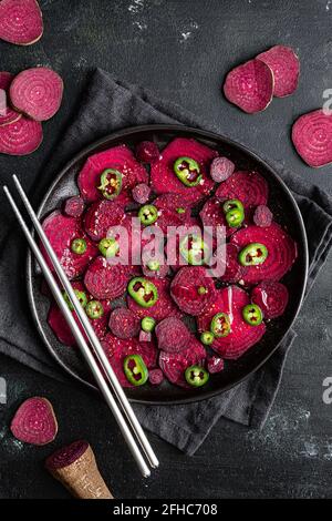 Top view composition of tasty beetroot slices arranged on baking pan with green jalapeno peppers and placed on black towel on kitchen table close to c Stock Photo