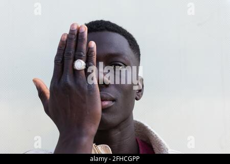 Handsome African American male covering half of face with hand and looking at camera on white background Stock Photo