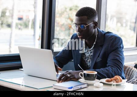 Serious African American male entrepreneur sitting at table in cafe and browsing netbook while working on project remotely Stock Photo