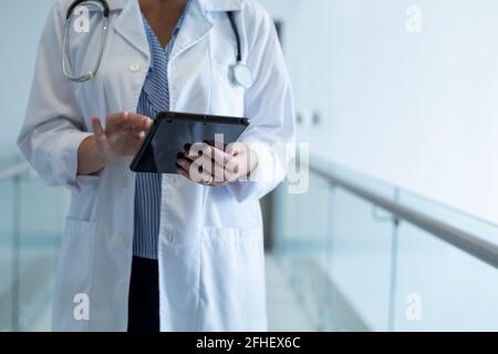 Midsection of caucasian female doctor standing in hospital corridor using digital tablet Stock Photo