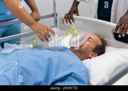 Diverse male and female doctors putting oxygen mask on patient lying in bed Stock Photo