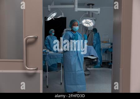Diverse group of male and female doctors in operating theatre wearing face masks performing surgery Stock Photo