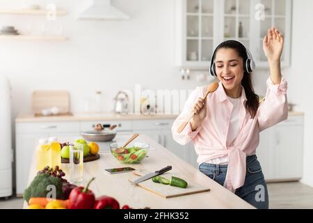 Portrait of smiling young woman singing and dancing in kitchen Stock Photo