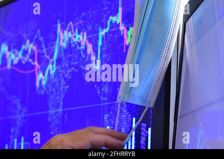 Disposable face mask on blurred background of computer screen and monitor with stock chart Stock Photo