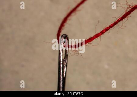 a red thread is threaded into a sewing needle Stock Photo