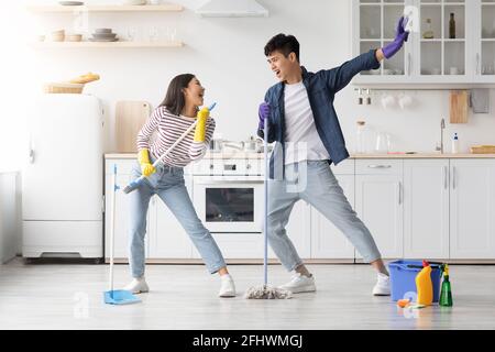 Funny asian couple singing songs while cleaning kitchen, copy space Stock Photo