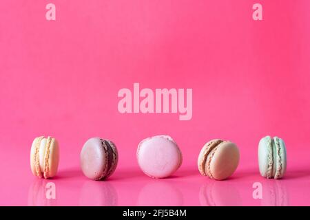 Close Up Fresh Colorful Macaroons In A Row Isolated On Pink Background, Sweet Colorful Biscuits Heap Lined Up With Reflection On Table Stock Photo