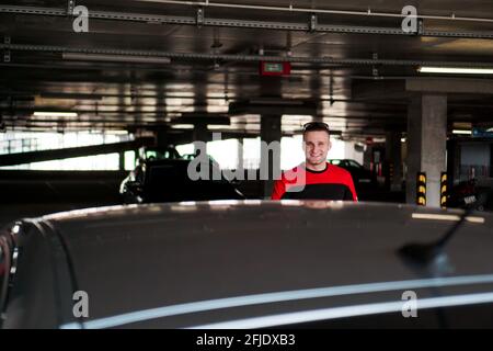 A young man in a tracksuit stands next to a car in an underground parking lot Stock Photo