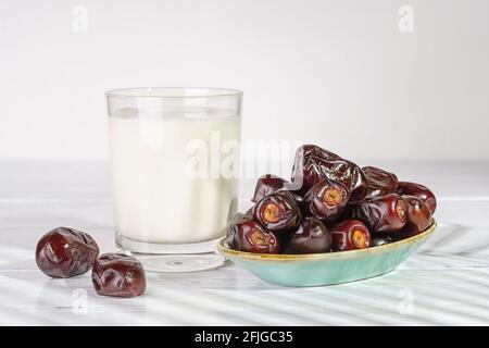 Delicious dried dates on a blue plate and glass of milk on a white wooden table. Vegetarian, dieting, healthy food ingredient. Organic Iranian dates. Stock Photo