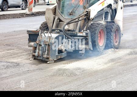 Compact road tractor with hydraulic attachment cuts cracks when repairing road foundations. Stock Photo