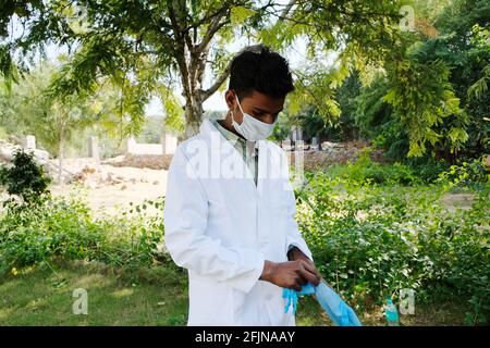 A young Indian health care worker in a medical face mask putting on latex gloves in a park Stock Photo