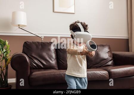 Boy wearing virtual reality headset using controller while exploring cyberspace in living room Stock Photo