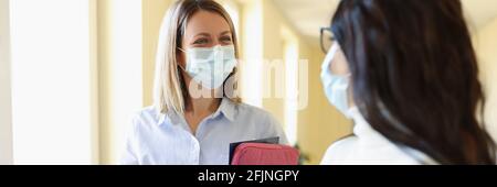 Two businesswoman in medical protective masks are talking in office. Stock Photo