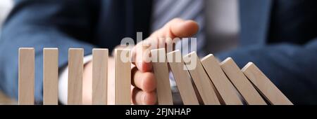 Business man in suit holding with hand falling sequence of wooden blocks Stock Photo