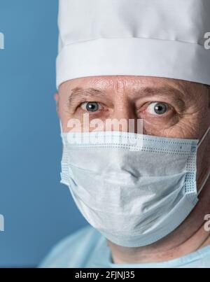 Portrait of a surprised elderly doctor, a man in medical clothes: a cap and a mask. Close-up, look at the camera Stock Photo