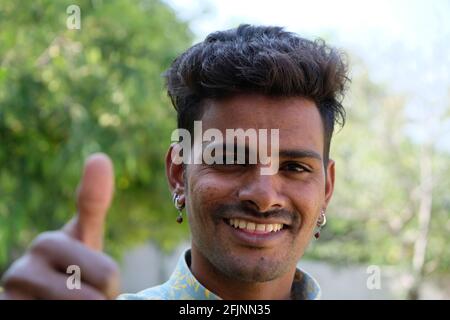 A portrait of a happy smiling Indian male standing in a park showing thumbs up Stock Photo