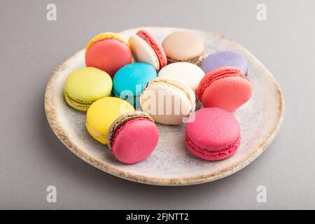 Multicolored macaroons on ceramic plate on gray pastel background. side view, close up, still life. Breakfast, morning, concept. Stock Photo